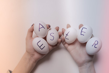 White eggs with Easter inscription in female hands on a light background