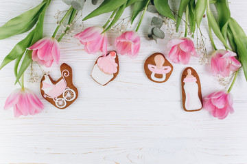 A composition for newborns on a wooden white background with pink tulips, hearts and a cookies. It's a girl.