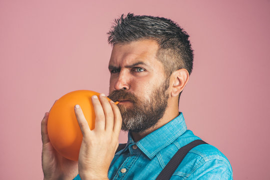 Concept for happy birthday, celebration - happy father is blowing orange balloon. Handsome bearded man holding air balloon in hands. Stylish man with beard and mustache inflating balloon.