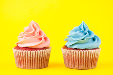 Cupcake red velvet with blue and pink whipped cream on yellow background. Picture for a menu or a confectionery catalog. Top view.