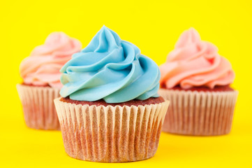 Cupcake red velvet with blue and pink whipped cream on yellow background. Picture for a menu or a confectionery catalog. Top view.