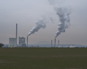 Fototapeta na wymiar thermal power station with smoking chimney in winter evening green grass foreground