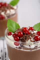 Chocolate mousse with currant and mint in a glasses on a whiite wooden background.