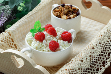 Homemade breakfast: cottage cheese with fresh raspberries and granola. In a white porcelain bowl, on a wooden tray