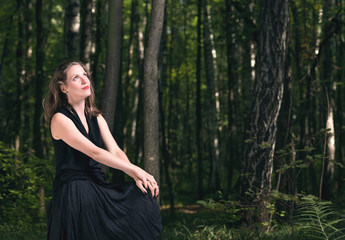Man alone with nature forest. Portrait of a young woman in a black dress sitting in the woods