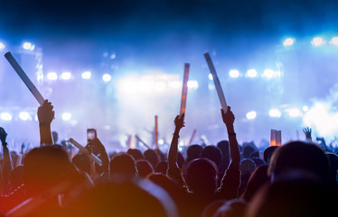 Crowd of concert stage lights and people fan audience silhouette raising hands or glow stick...
