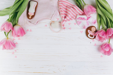 Obraz na płótnie Canvas A composition for newborns on a wooden white background with clothes, pink tulips, hearts and a cookies, copy space and flat lay. It's a girl.