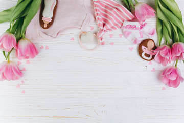 A composition for newborns on a wooden white background with clothes, pink tulips, hearts and a cookies, copy space and flat lay. It's a girl. - obrazy, fototapety, plakaty
