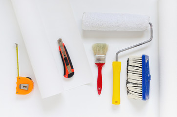 house repair equipment, white wallpaper roll with paint roller, brush, tape measure, knife