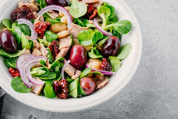 salad with white beans, tuna, olives, red onions and dried tomatoes with green lettuce leaves