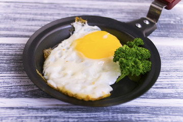 fried egg in a frying pan with greens on a wooden background
