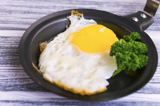 fried egg in a frying pan with greens on a wooden background