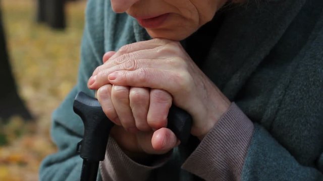Sad lonely elderly woman dreaming about her past, poor life leaning wooden stick