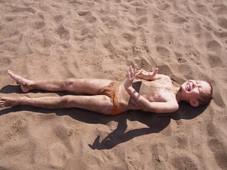 Muddy boy lies on sand at the beach © relena74