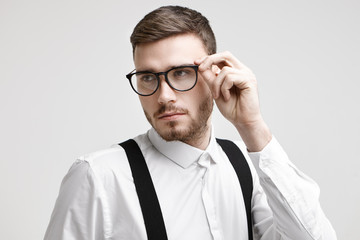 Fototapeta na wymiar People, style, optics and eyewear concept. Horizontal picture of confident handsome young unshaven European male wearing white formal shirt with black suspenders, adjusting stylish spectacles
