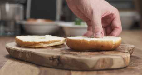 Obraz na płótnie Canvas Man hands making bagel sandwich on wood board