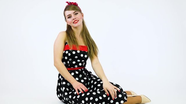 A beautiful 50s pin-up girl sits on the floor, smiles at the camera and moves in rhythm of music - white background