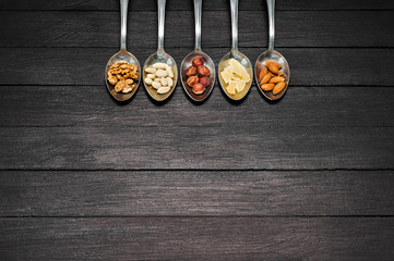 Different kinds of nuts. On a dark wooden table lie spoons with nuts of almonds, walnuts, hazelnuts, dried pineapples, peanuts.