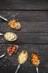 Various beans and different kinds of nuts. On a dark wooden table lie spoons with nuts of almonds, walnuts, hazelnuts, dried pineapples, peanuts. The table is strewn with seeds of flax and sesame.