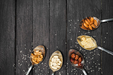 Different kinds of nuts. On a dark wooden table lie spoons with nuts of almonds, walnuts, hazelnuts, dried pineapples, peanuts. The table is strewn with seeds of flax and sesame.