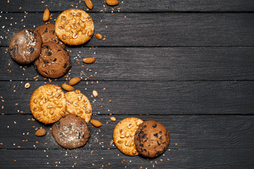 Freshly baked chocolate biscuits on a wooden table. On the table is a board, a glass of milk, around various nuts, sesame, flax, almonds. View from above.