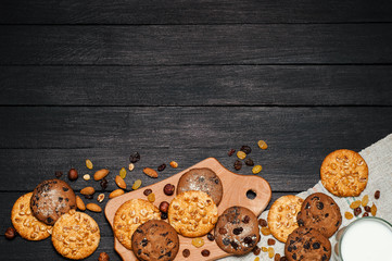 Freshly baked cookies on a wooden table. On the table is a board, a glass of milk, around various nuts, almonds and raisins.