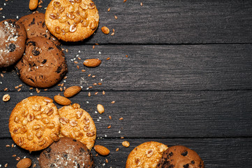 Freshly baked chocolate biscuits on a wooden table. On the table is a board, a glass of milk, around various nuts, sesame, flax, almonds.