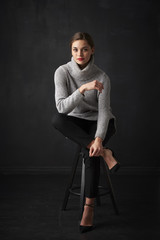 Fototapeta na wymiar Relaxed young woman at dark background. Full length shot of attractive young woman wearing turtleneck sweater while sitting at dark background and relaxing. 