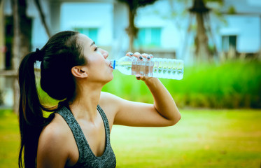 A women drinking water from bottle in a park.