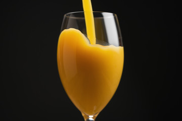 pouring orange juice into glass over black background