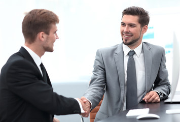 handshake of business partners sitting at a Desk.