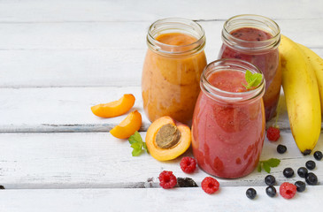 Orange, red and purple smoothies of fresh ingredients - bananas, apricots, raspberries and blueberries on a light background. Healthy food concept. Vegetarian product. Organic Raw Drink. Copy space.