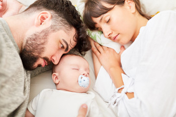 Fototapeta na wymiar Eltern liegen entspannt mit Baby auf dem Bett