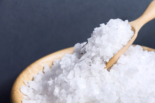 Sea salt white crystals on wooden spoon in wooden bowl isolated on the gray background.