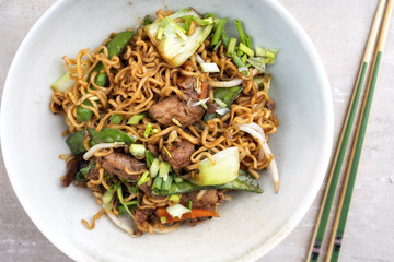 Traditional stir-fried Thai phat mama mie noodles with pork and vegetables as top view in a bowl