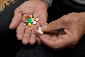 An elderly man holds a lot of colored pills in old hands. Painful old age. Health care of older people