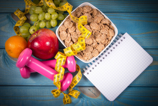 Diet fitness concept - dumbbells, measuring tape, flakes and fresh fruits on wooden table.