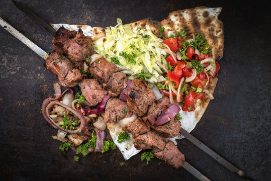 Traditional Greek souvlaki barbecue skewer with cabbage and tomato onion salad as top view on phyllo bread with copy space