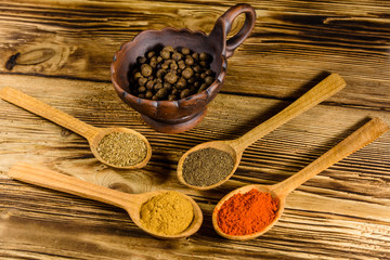 Ceramic bowl and spoons with the different spices on wooden table