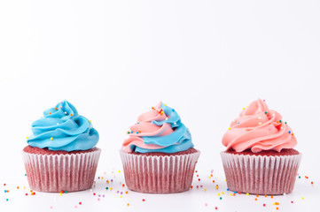 Cupcake red velvet with blue and pink whipped cream decorated with colorful sprinkles on white background.