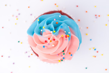 Cupcake red velvet with blue and pink whipped cream decorated with colorful sprinkles on white background. Top view.