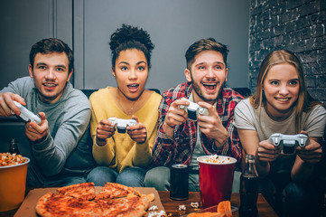 Close up of four friends sitting together and playing the game. All of them want to win. They are...