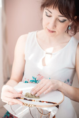 Young beautiful woman is engaged in embroidering a dagger on the embroidery frame in a colored...