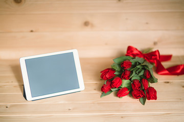 Beautiful red tulips and tablet on a wooden background