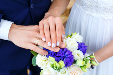 Bridal bouquet and wedding rings on the hands of the bride and groom