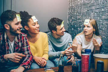 Another picture of teens playing the words game where the blode girl is trying to duggest what word is written in her piece of paper. Her friends are listening to her very careful