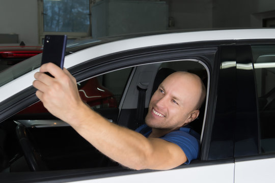 Young car service technician sit in the car and make self photo.