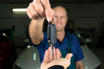 Young car service technician give key of car to customer.