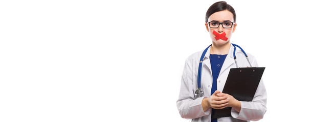 Young woman doctor with stethoscope holding clipboard in her hands with taped lips in white uniform on white background