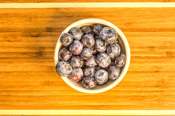 Fresh blueberries in a white ceramic bowl on a bamboo tray and white strips